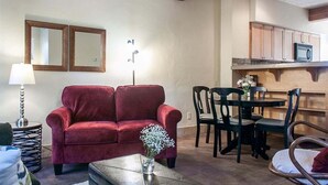 A living room with a red sofa, a coffee table with a vase, and a dining area with chairs and a table. - Bluebird Day - Casa Sol: Cozy 2BR townhome in Bend, OR, featuring two King beds and a hot tub. (Bend)