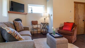 Una sala de estar con un sofá, un sillón rojo, una mesita con una lámpara y un televisor montado en la pared.
