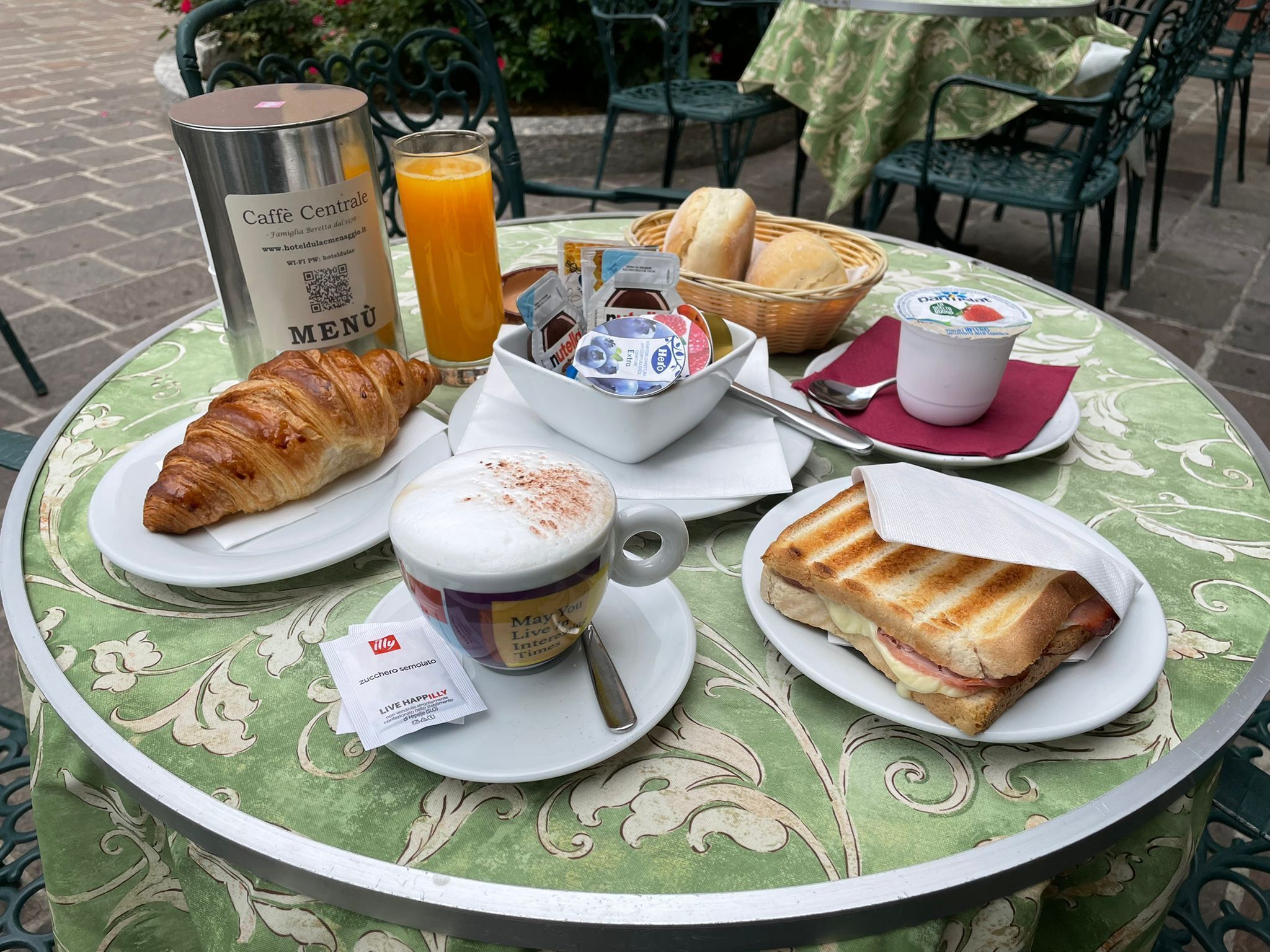 A table set with croissants, a sandwich, a cup of coffee, a glass of orange juice, and a menu.