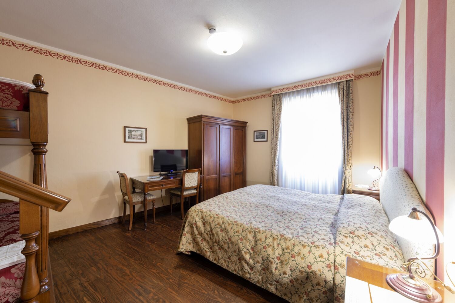 A hotel room with a bed, desk, chair, wardrobe, and a television.