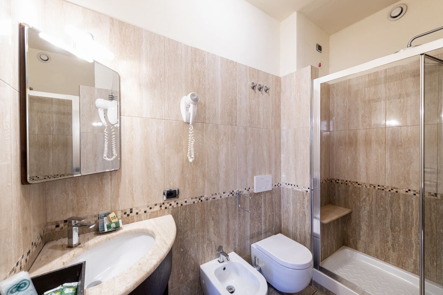 A modern bathroom with a vanity, bidet, toilet, and a glass-enclosed shower area.