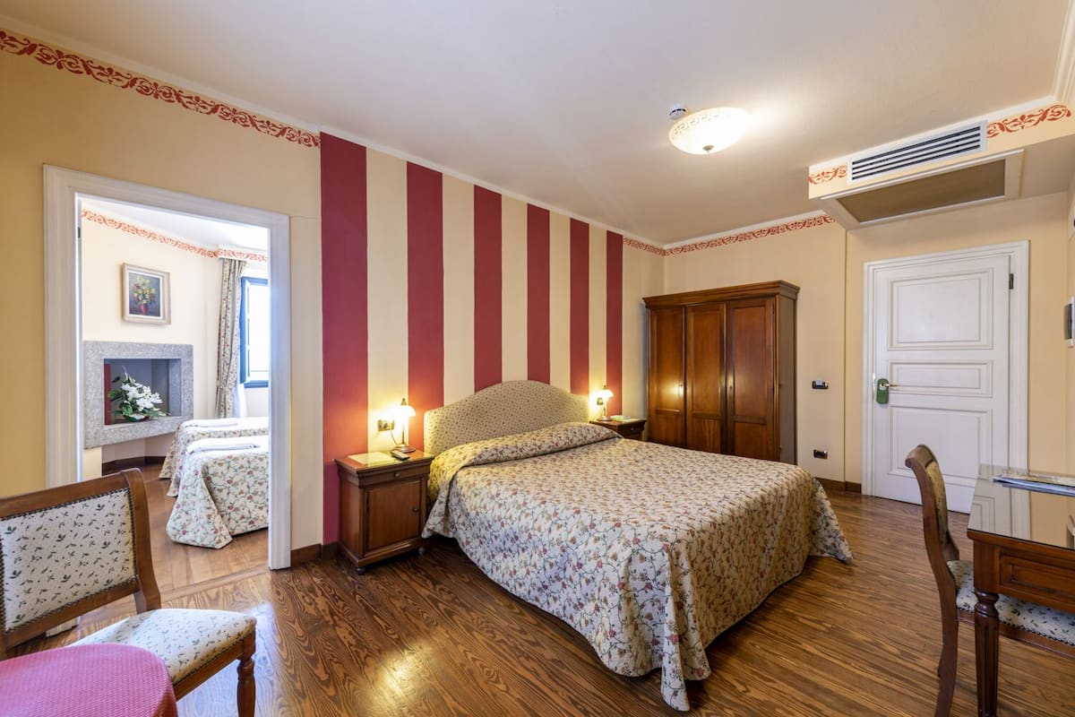 A bedroom with a bed, two bedside tables, a wardrobe, a mirror, a chair, and a small table.
