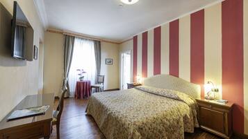 Ein Schlafzimmer mit einem Bett, einem Schreibtisch, einem Stuhl, einem Tisch mit Blumen und einem Fernseher an der Wand.