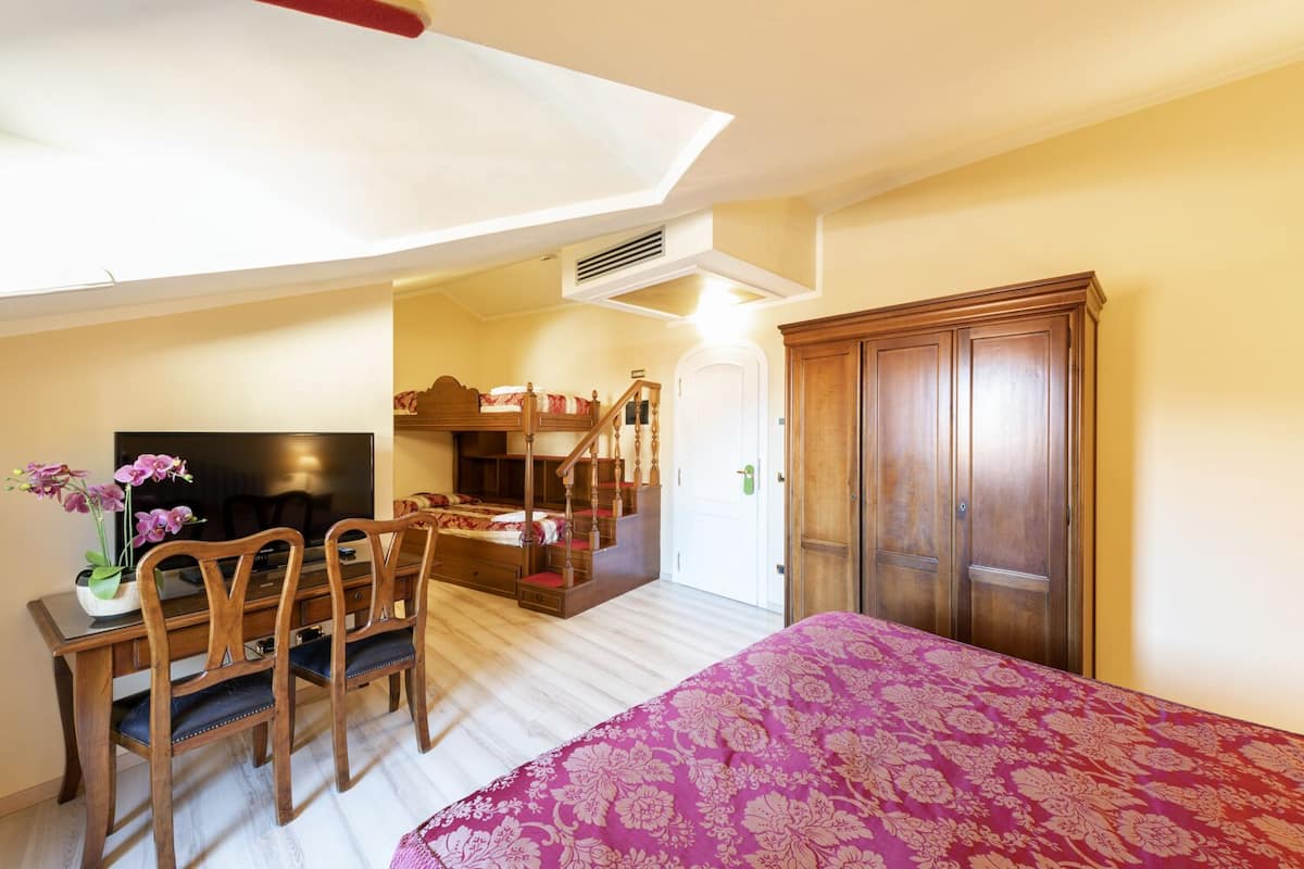 A bedroom with a bunk bed, a desk with a chair, a television, and a wardrobe.