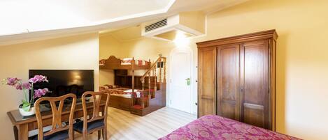 A bedroom with a bunk bed, a desk with a chair, a television, and a wardrobe.
