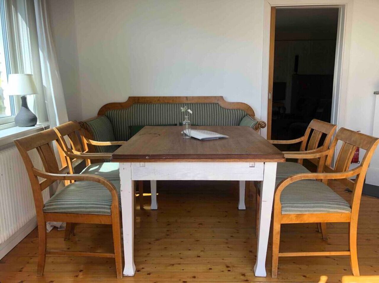 Ett matrum med ett träbord, sex stolar, en bänk och ett fönster med en lampa.