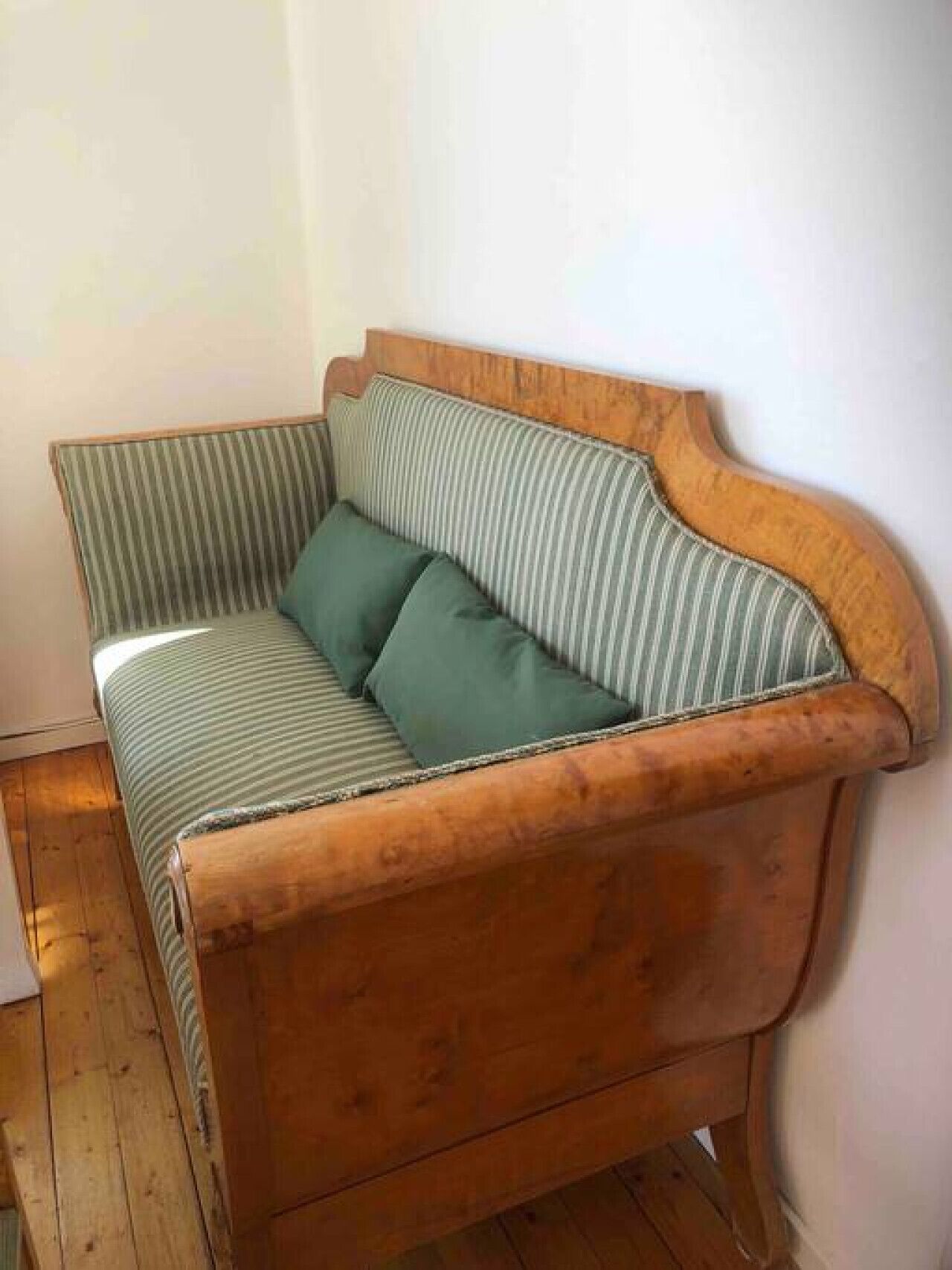 A wooden sofa with a striped cushion, positioned against a plain wall.