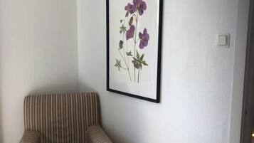 En randig fåtölj i ett hörn, med en inramad botanisk tavla på väggen.