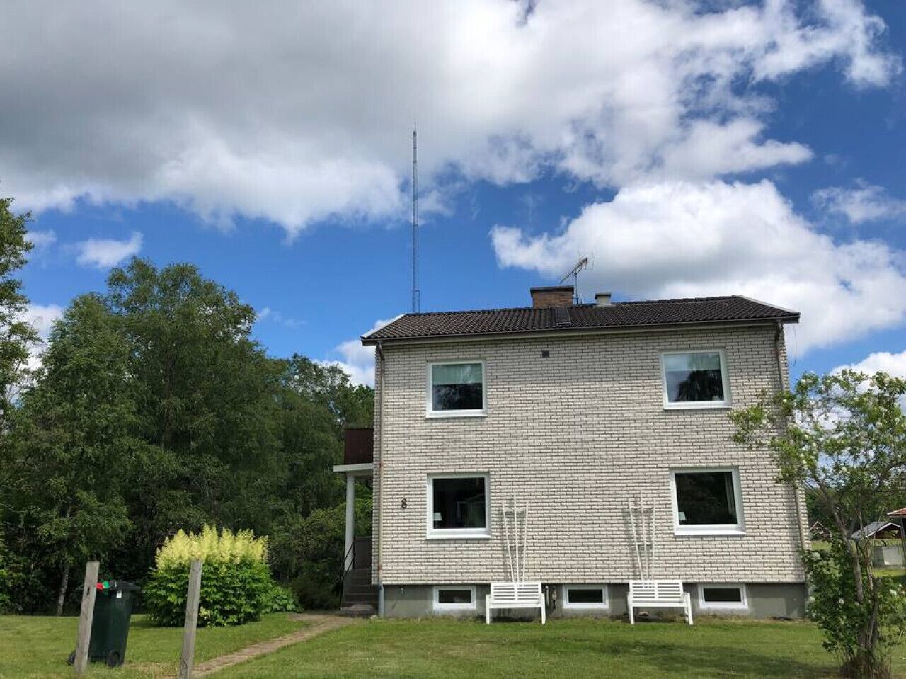 Een tweelaags huis met een bakstenen gevel, schoorsteen en schotelantenne.