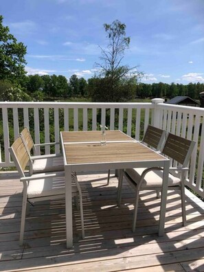 Una terraza con mesa y sillas, rodeada por una barandilla blanca, con vistas a un paisaje verde.