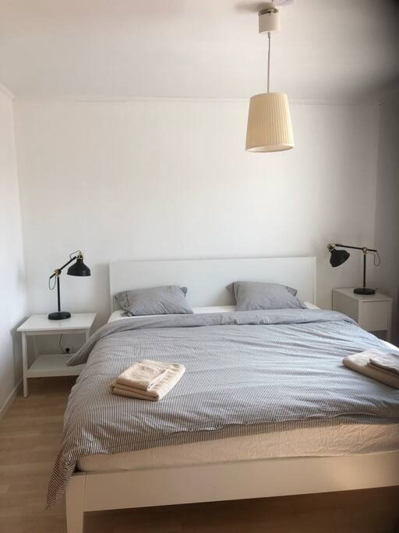 Ett minimalistiskt sovrum med en säng, två sängbord, en hängande lampa och en enkel vägg.