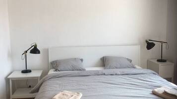 Ett minimalistiskt sovrum med en säng, två sängbord, en hängande lampa och en enkel vägg.