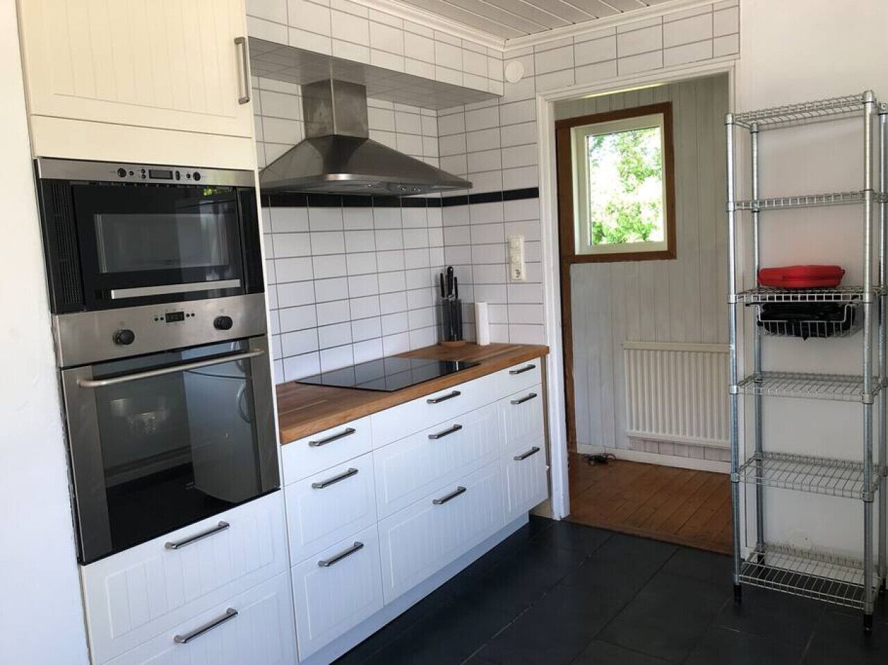 Une cuisine avec des meubles blancs, un plan de travail noir, des appareils en acier inoxydable et une étagère en métal.