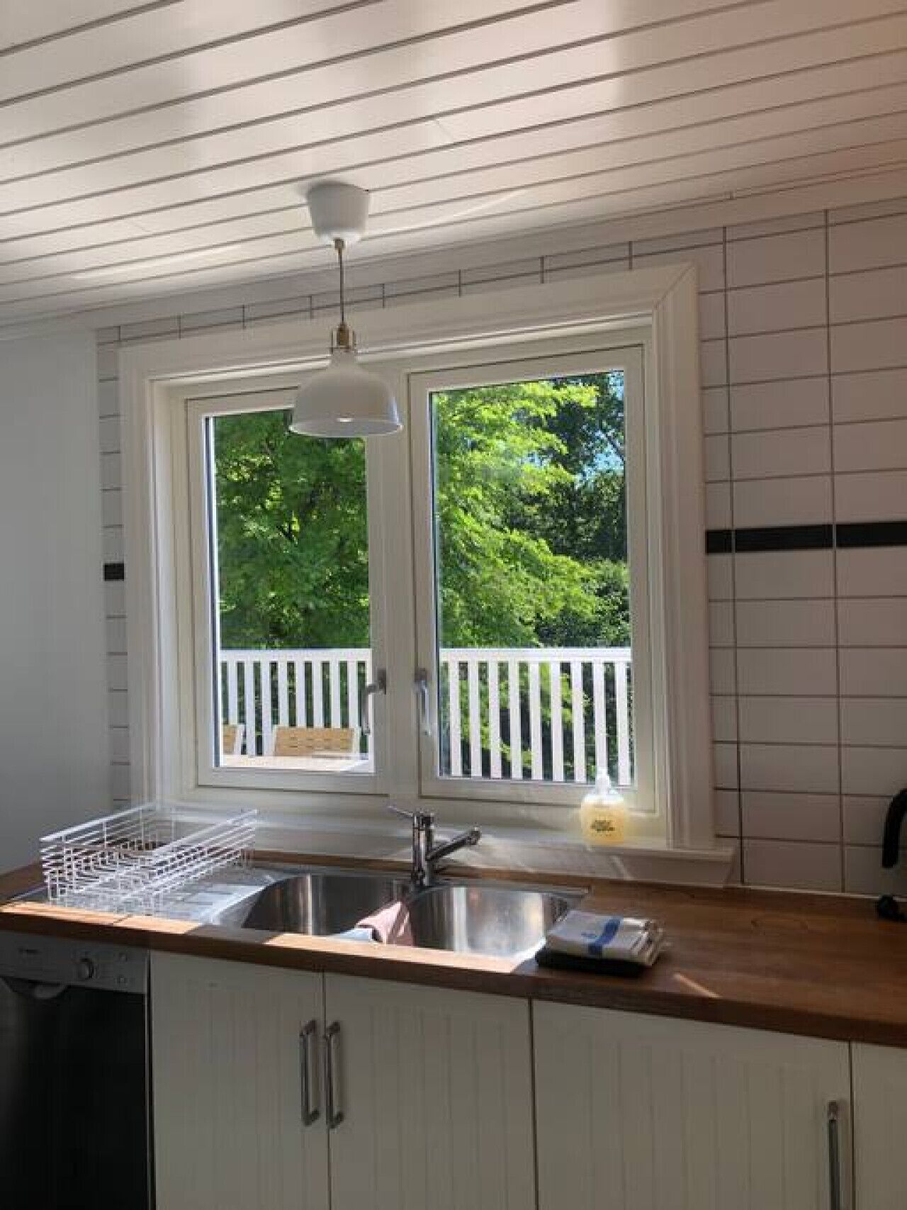 Una cocina con un lavamanos doble, armarios blancos, encimera de madera y vista a un balcón con barandillas blancas.