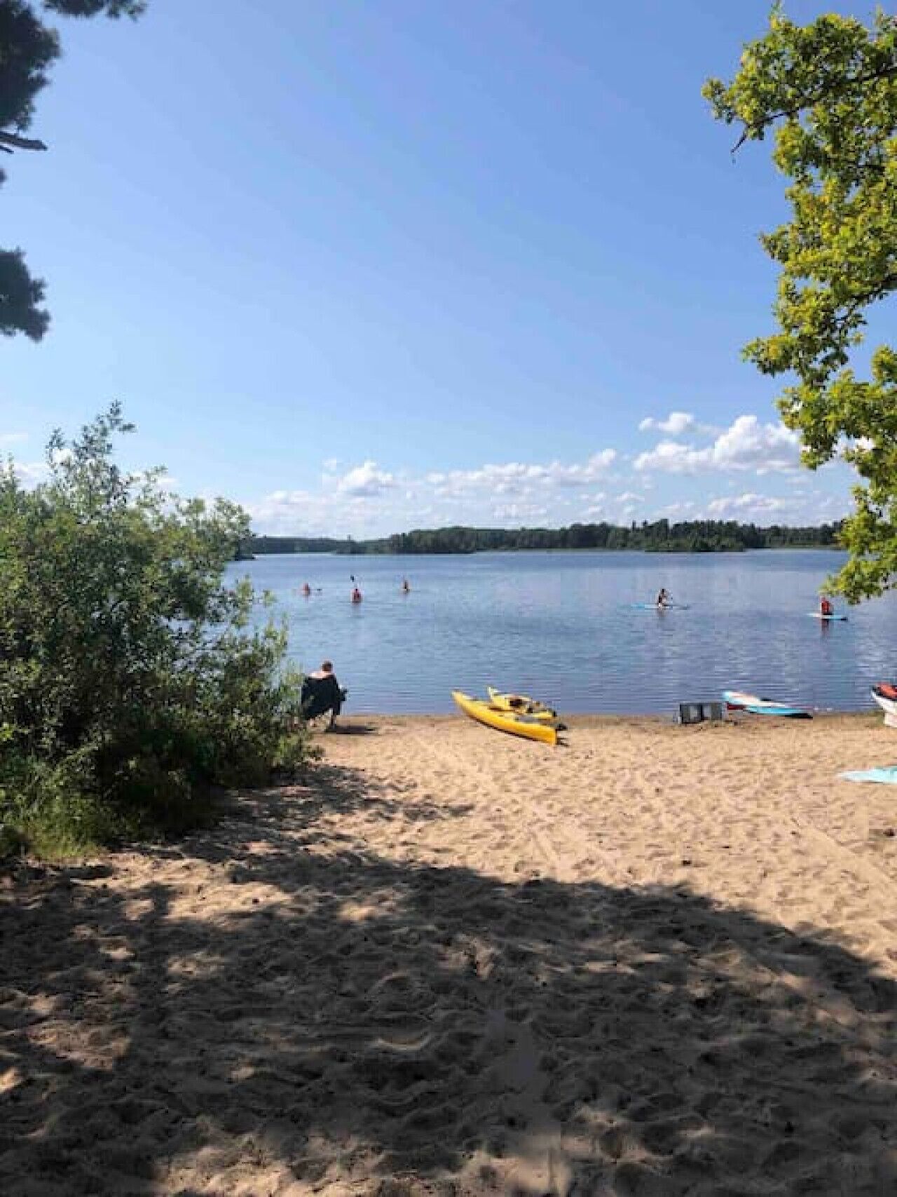 A sandy beach with kayaks and a calm lake.