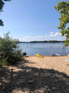 A sandy beach with kayaks and a calm lake.