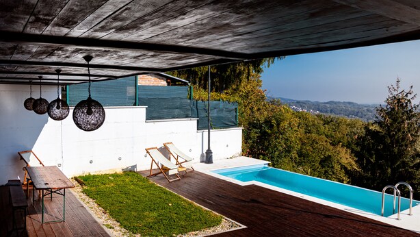 Ein moderner Außenpoolbereich mit Holzterrasse, zwei Liegestühlen und Blick auf die umliegende Landschaft.