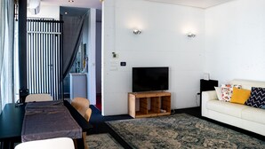 Ein modernes Wohnzimmer mit einer Couch, einem Fernseher auf einem Holzboden, einem Esstisch und einem gemusterten Teppich.