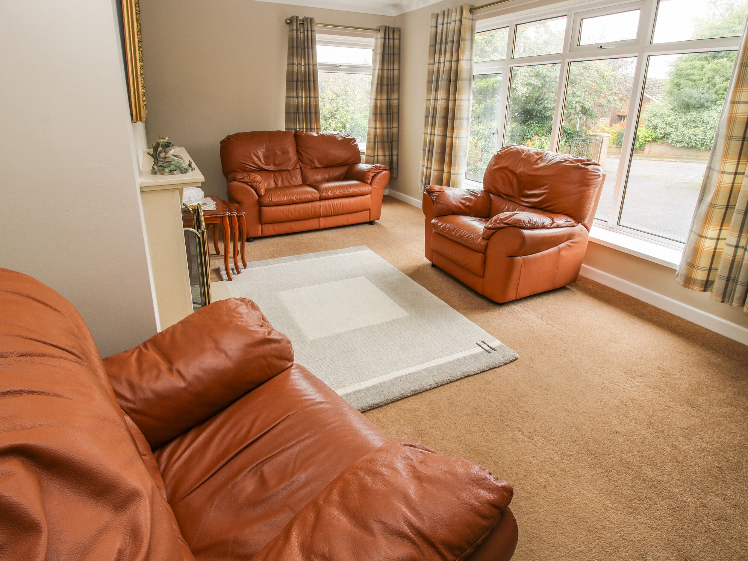 A living room with two brown leather sofas, a white rug, and a view of the outdoors through large windows.