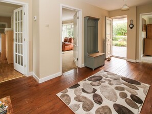 A spacious hallway with wooden flooring, a patterned rug, and a bench.