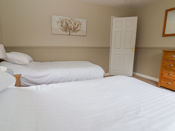 A hotel room with two single beds, a wooden dresser, a door, and a wall-mounted artwork.