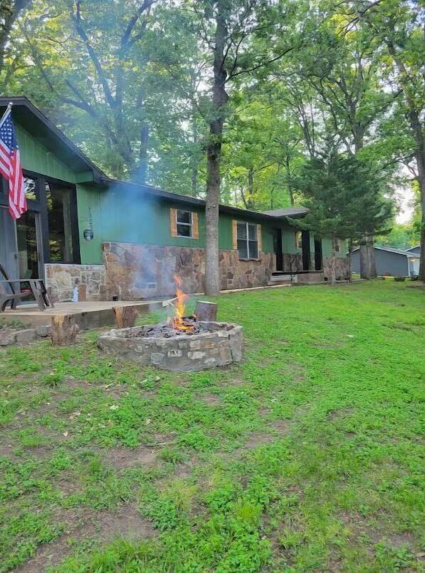 A rustic cabin with a stone fire pit in the yard, surrounded by lush greenery and trees. - Spohn-taneous Retreat (Grove)