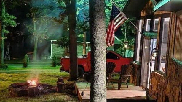 Eine rustikale Holzhütte mit Feuerstelle, einer US-amerikanischen Flagge und einem roten Fahrzeug in der Nähe.