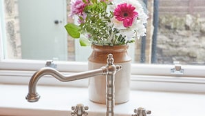Uma torneira de estilo antigo com um vaso de flores no parapeito de uma janela.