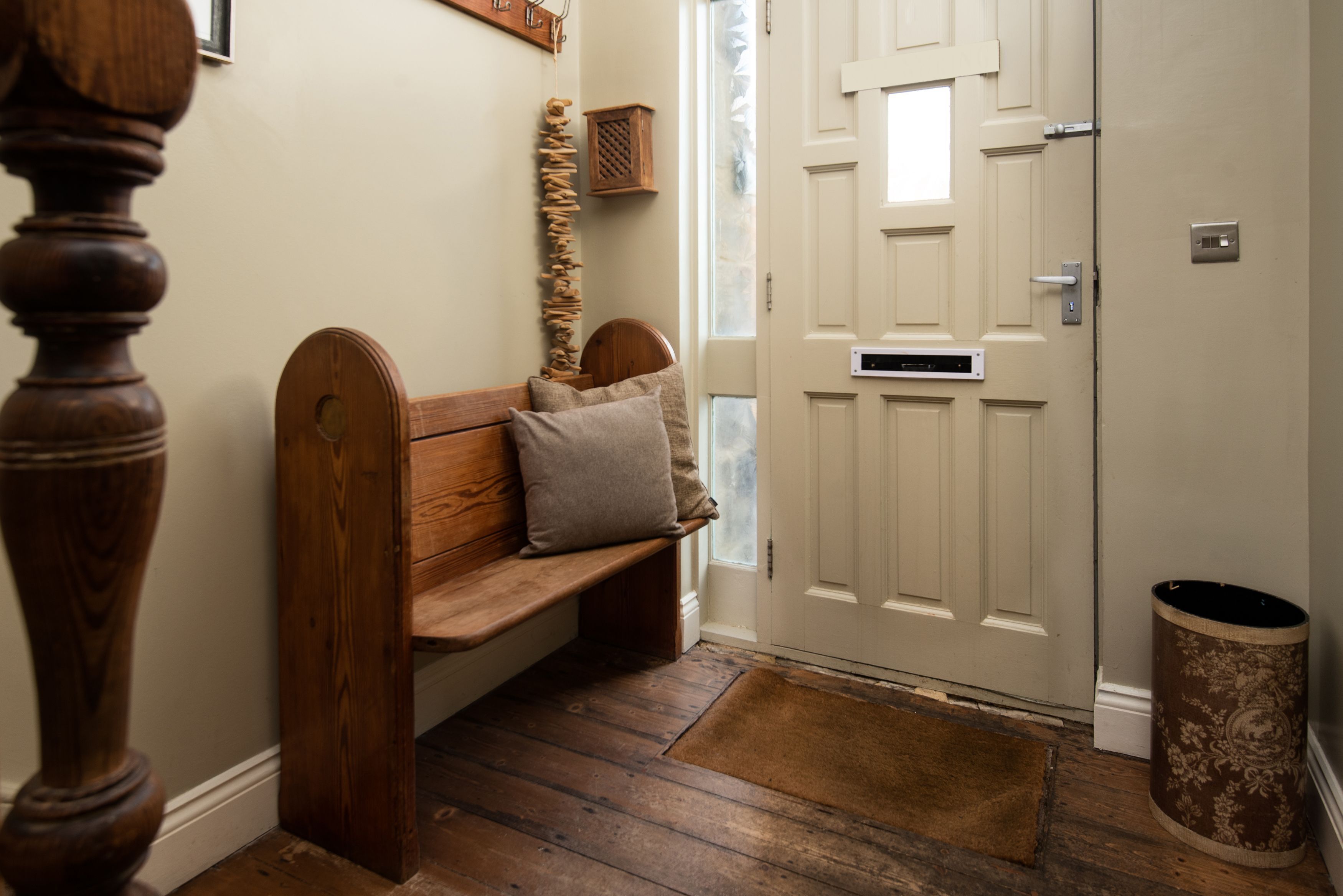 A wooden bench with cushions, a white door with a mail slot, and a trash can.