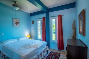 Quarto com cama, duas janelas com cortinas vermelhas, abajur e quadro na parede.