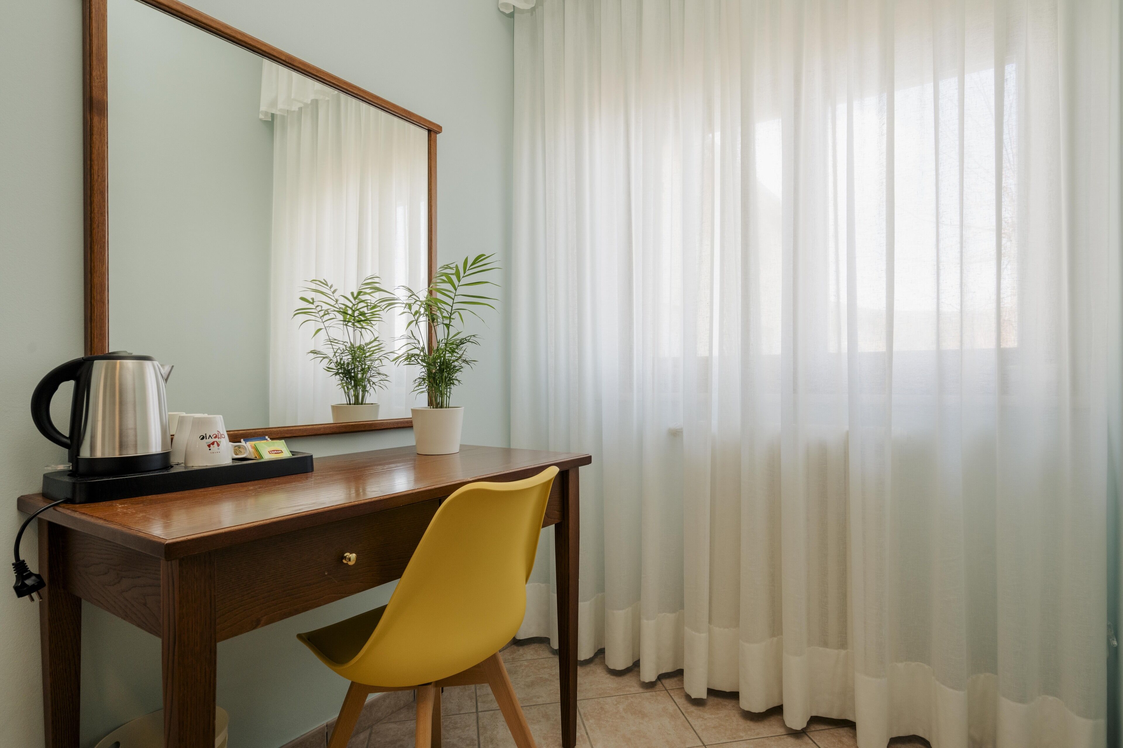 A room with a wooden desk, a yellow chair, a potted plant, a kettle, and a mirror.