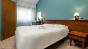 Habitación de hotel con una cama grande, una mesita de noche con lámpara, una mesita auxiliar de madera y un espejo en la pared.