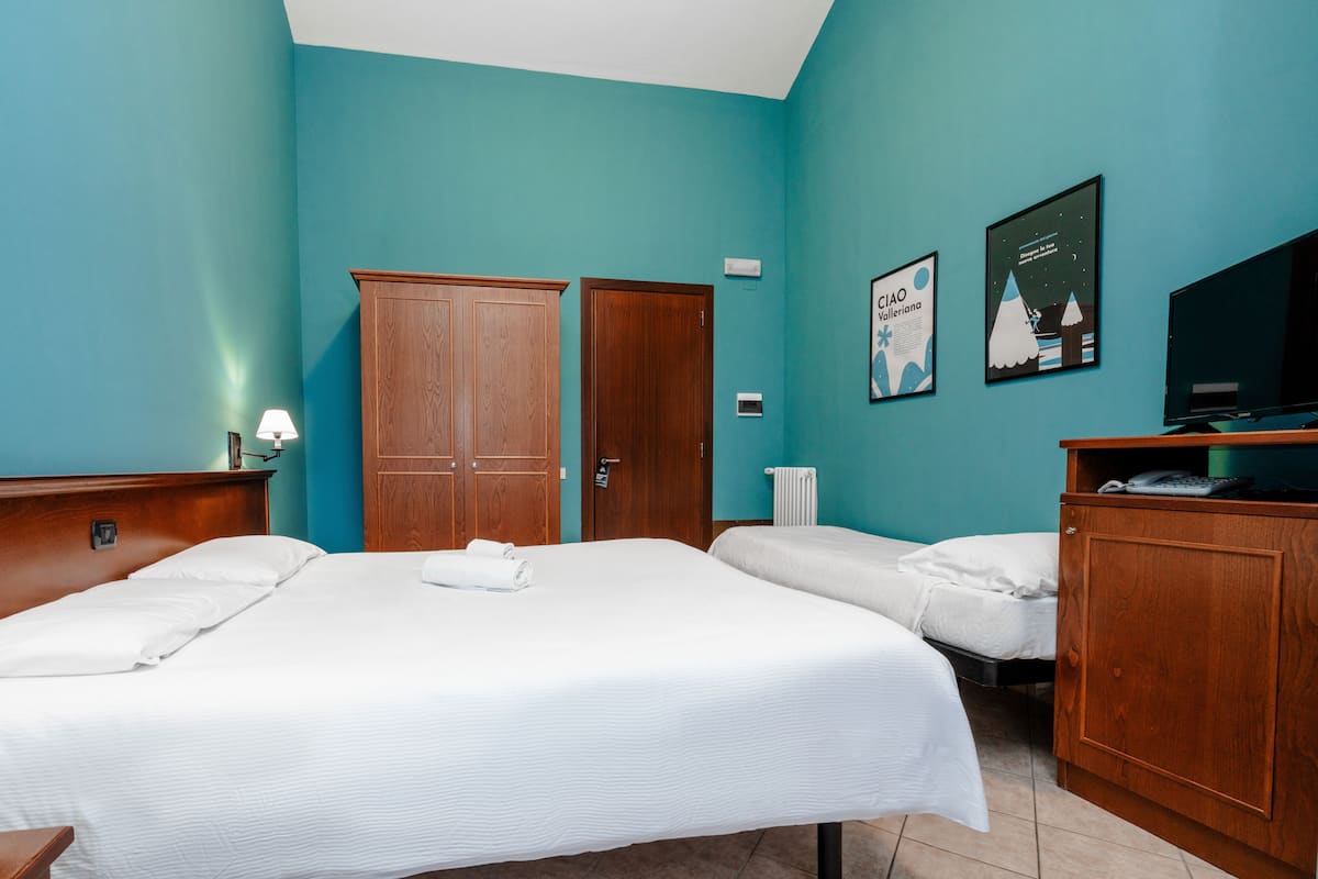 A hotel room with two beds, a wooden wardrobe, a television, and two wall posters.