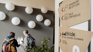 Un área de recepción con señales indicativas para 'Infopoint Reception' y 'Sala Conferencee', además de un cartel para 'Bar Sala Colazioni Ristorante'.