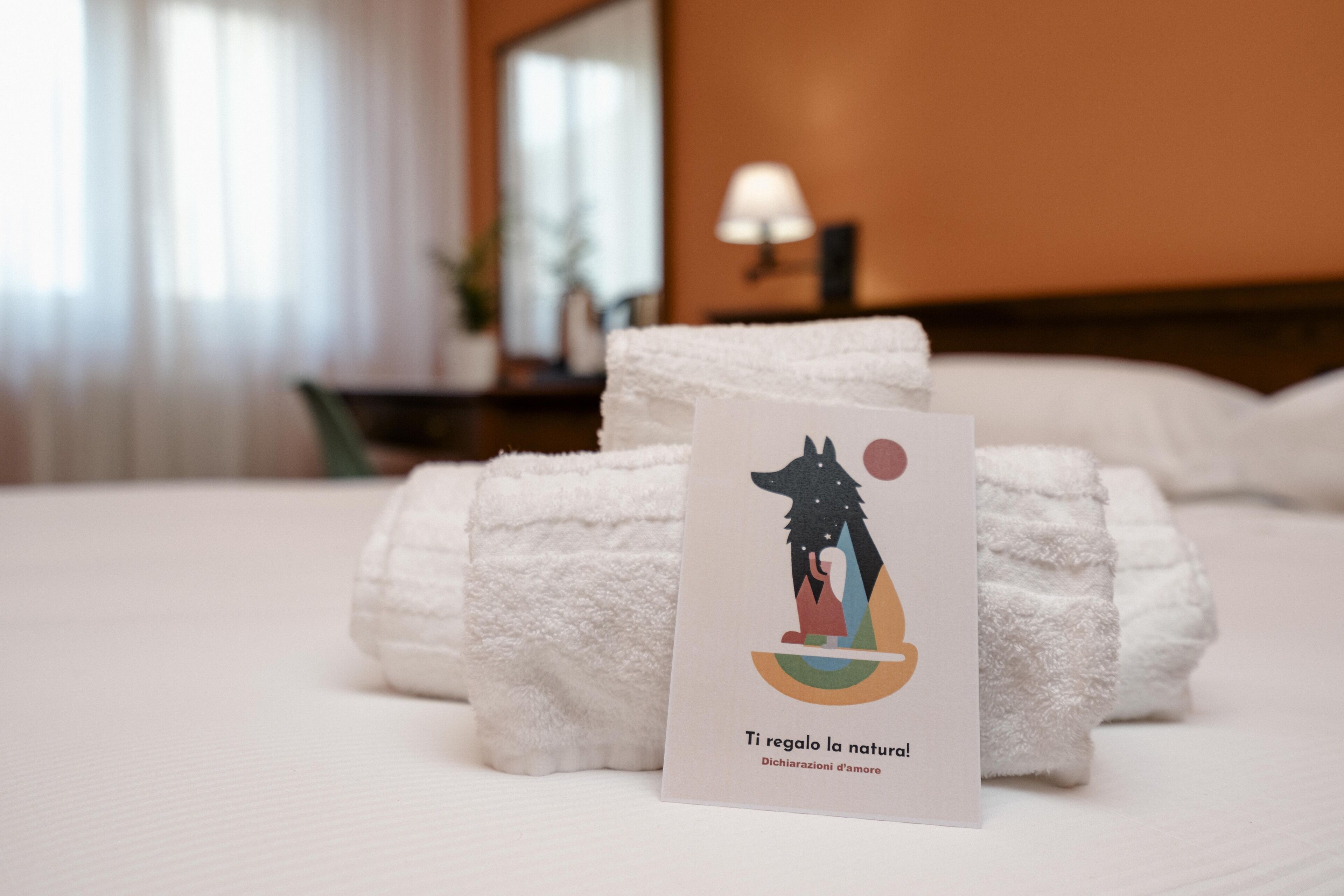 Una cama bien hecha con toallas blancas y una tarjeta con una ilustración de motivos naturales.