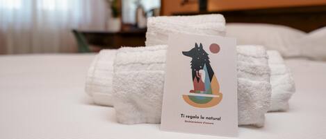 Una cama bien hecha con toallas blancas y una tarjeta con una ilustración de motivos naturales.