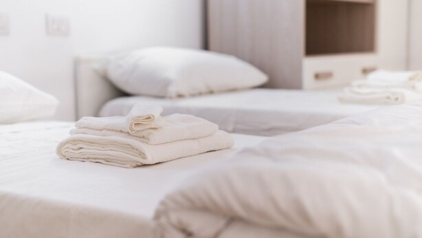 Una habitació d'hotel amb tovalloles netes i ben plegades als llits, una paret blanca i un armari de fusta.