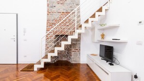 Una escala amb baranes blanques que condueix a una habitació amb una paret de maó i un televisor sobre un moble blanc.