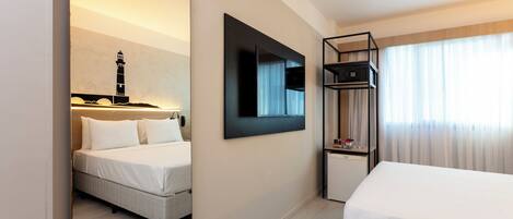 Una habitación de hotel con cama, escritorio, espejo, televisor y estante.