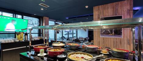 A buffet area with multiple hot food stations, a television screen, and a wooden accent wall.