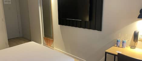A hotel room with a bed, a TV mounted on the wall, a desk with a telephone, and a minibar.