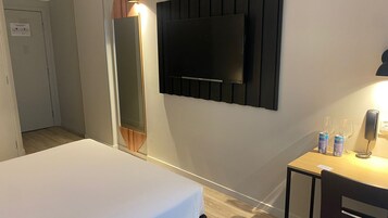 Habitación de hotel con cama, televisión montada en la pared, escritorio con teléfono y minibar.