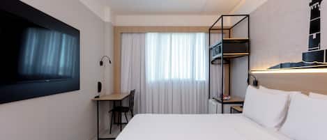 Una habitación de hotel con cama, escritorio, silla, televisión y un cuadro de un faro.