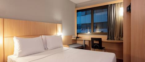 Una habitación de hotel con una cama grande, un escritorio con una silla y una ventana con cortinas.