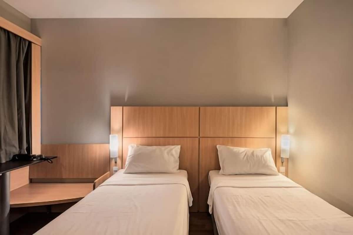 Habitación de hotel con dos camas, cabecero de madera, lámparas de noche y un escritorio con una silla.