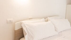 Un lit bien fait, avec du linge de lit blanc et une tête de lit en bois, dans une chambre d’hôtel.