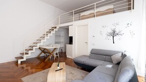 Un salon moderne avec un canapé gris, une table basse en bois et un escalier menant à un niveau supérieur.