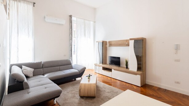 Un salon moderne avec un canapé d’angle gris, une table basse en bois et un téléviseur posé sur un meuble en bois.