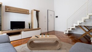 Un salon moderne avec un téléviseur à écran plat, des étagères en bois, un escalier et une table basse.