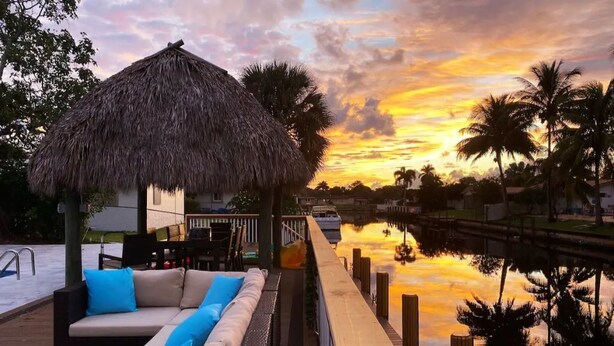 Eine Holzterrasse mit einer strohgedeckten Struktur, einem Pool und einer Lounge mit Kissen.
